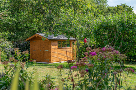 Superior Shed by Crane A Sikkens stained wooden shed in a large lawned garden, tucked behind some trees.